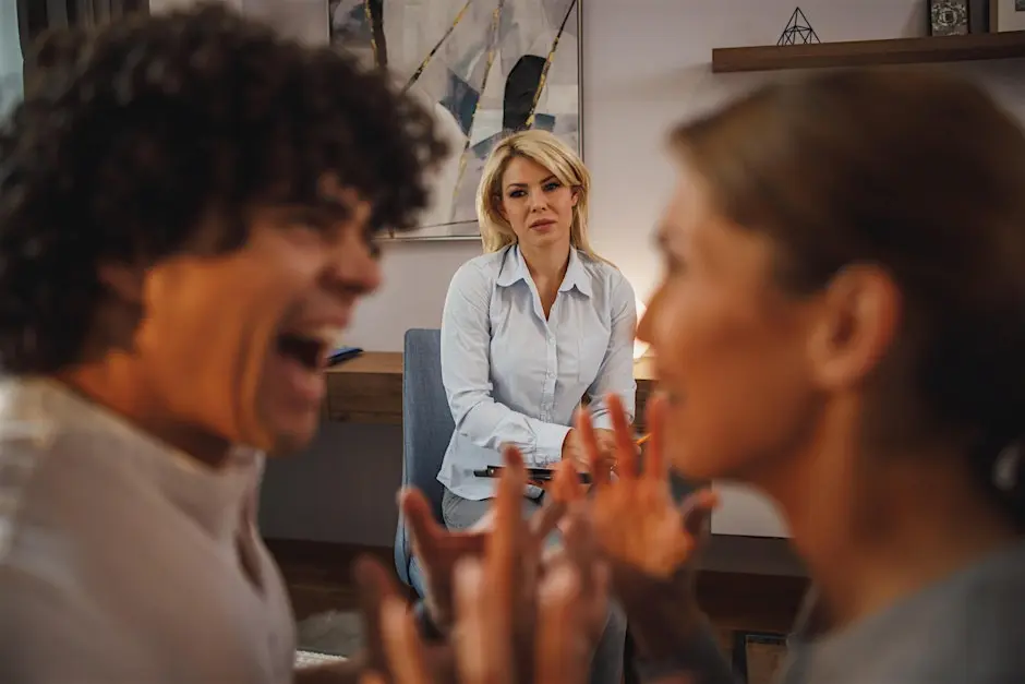 A therapist in a white shirt sits calmly between a man and a woman, who are energetically debating in the foreground. The scene suggests tension.
